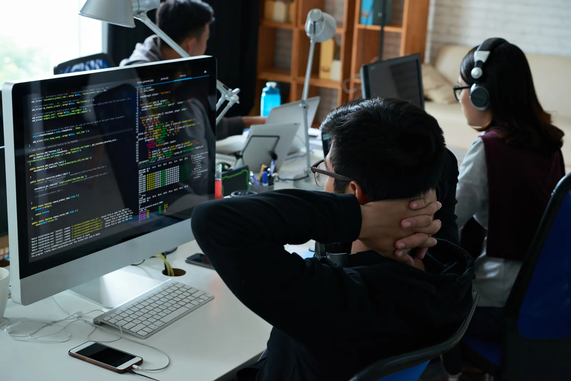 Developer reviewing code on monitor in busy office