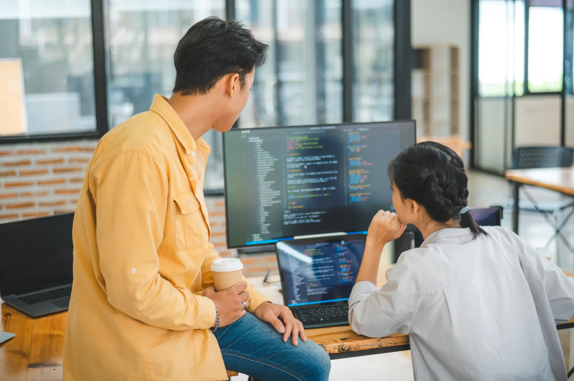 Two developers collaborating over code on dual screens