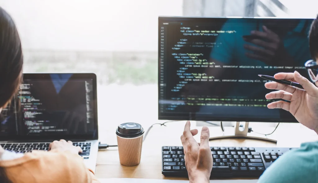 Two developers collaborating over code on multiple screens