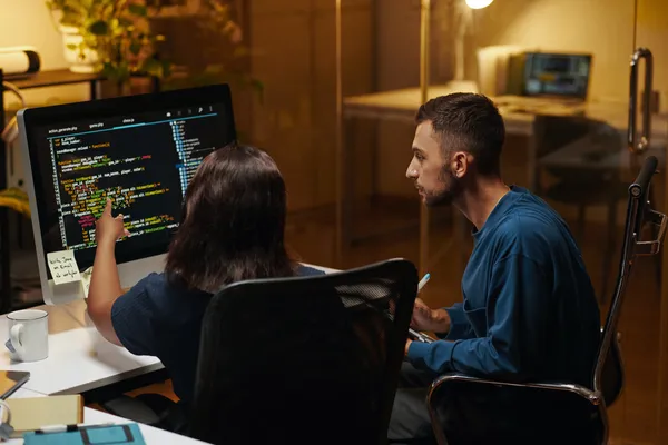 Two developers collaborating on code at a computer workstation