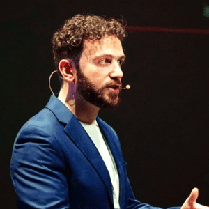 Man with beard speaking on stage with microphone